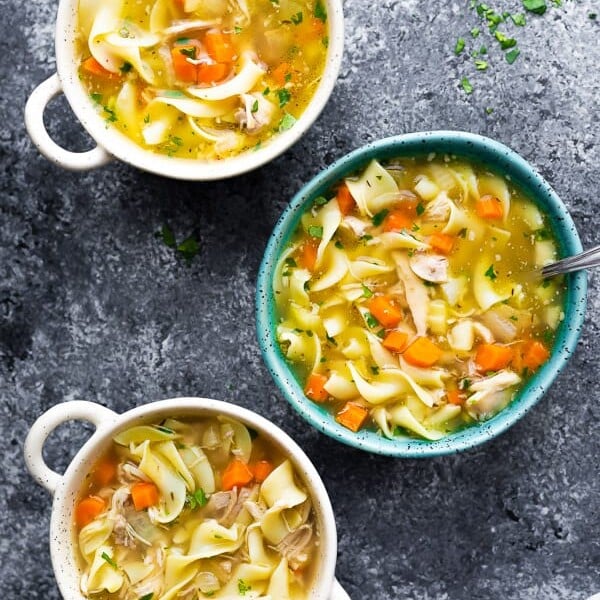 overhead shot of three white and blue bowls with chicken noodle soup