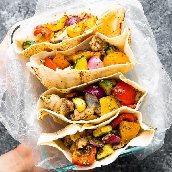 overhead shot of a hand holding up four pesto chicken pitas on parchment paper