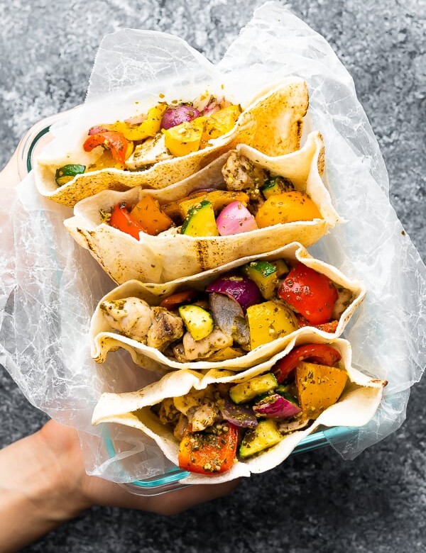 overhead shot of a hand holding up four pesto chicken pitas on parchment paper