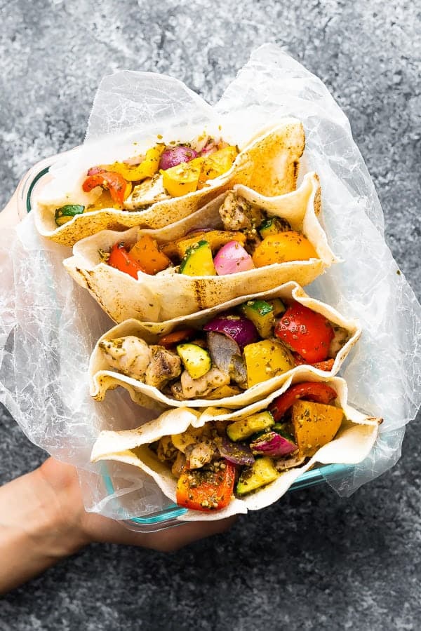 overhead shot of a hand holding up four pesto chicken pitas on parchment paper