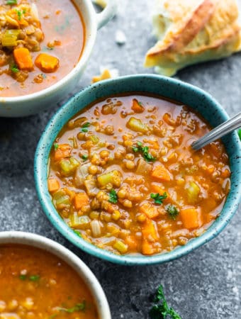 three bowls filled with hearty lentil soup with a spoon and bread in the background