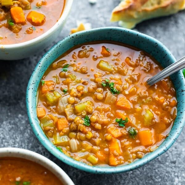 three bowls filled with hearty lentil soup with a spoon and bread in the background