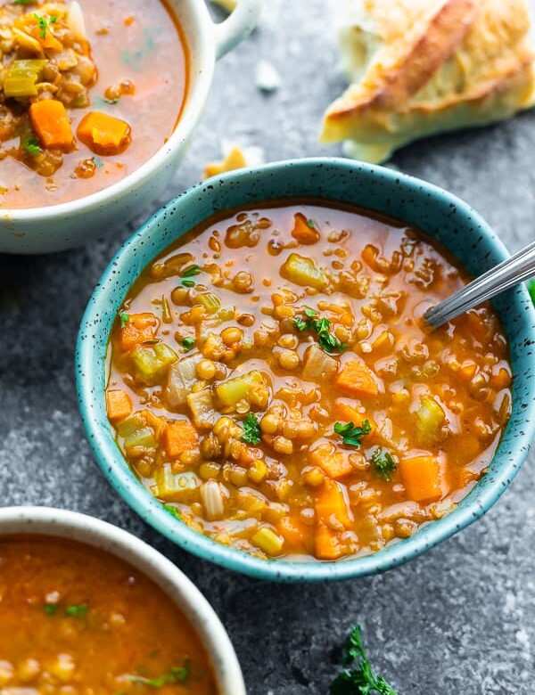 three bowls filled with hearty lentil soup with a spoon and bread in the background