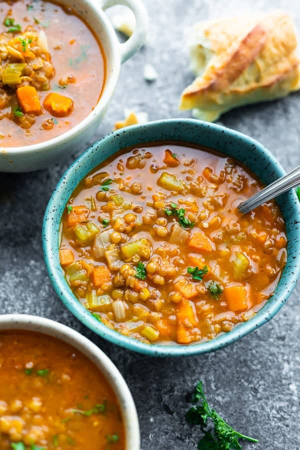 three bowls filled with hearty lentil soup with a spoon and bread in the background