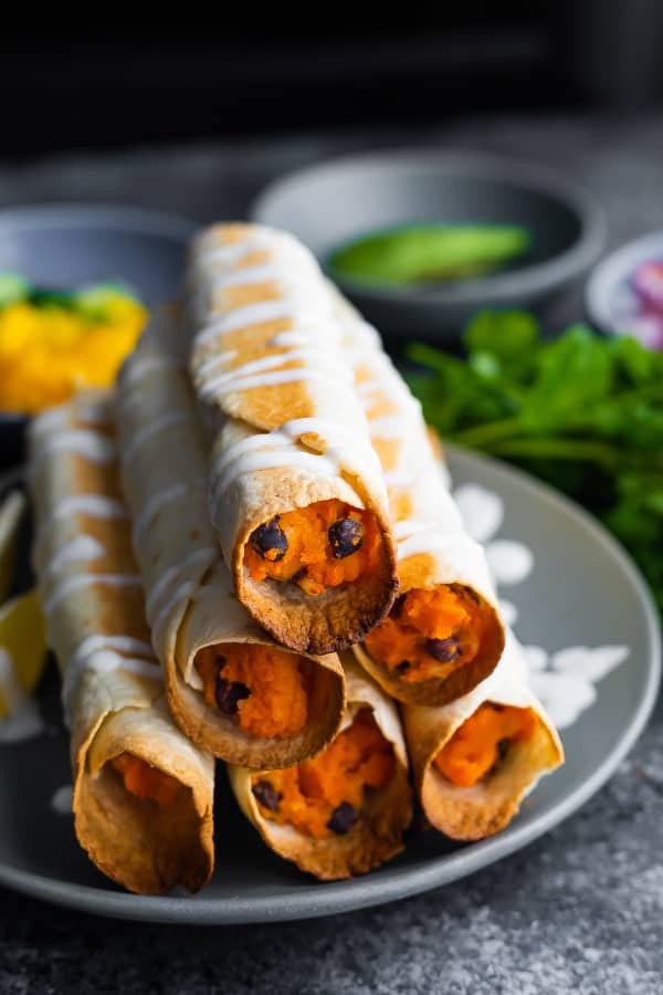 baked taquitos with black beans and sweet potatoes on plate drizzled with yogurt
