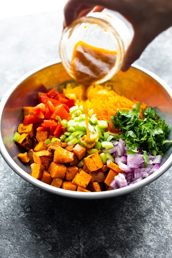 pouring vinaigrette over sweet potato salad