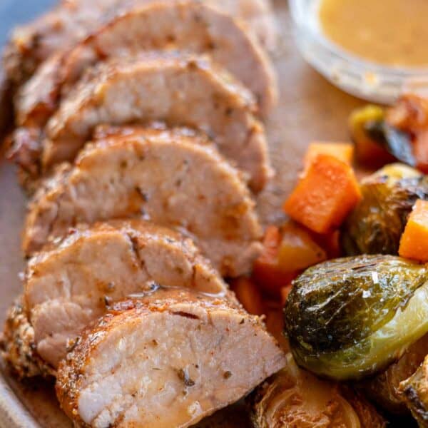 a closeup shot of a roasted pork tenderloin with juice on the plate and vegetables on the side