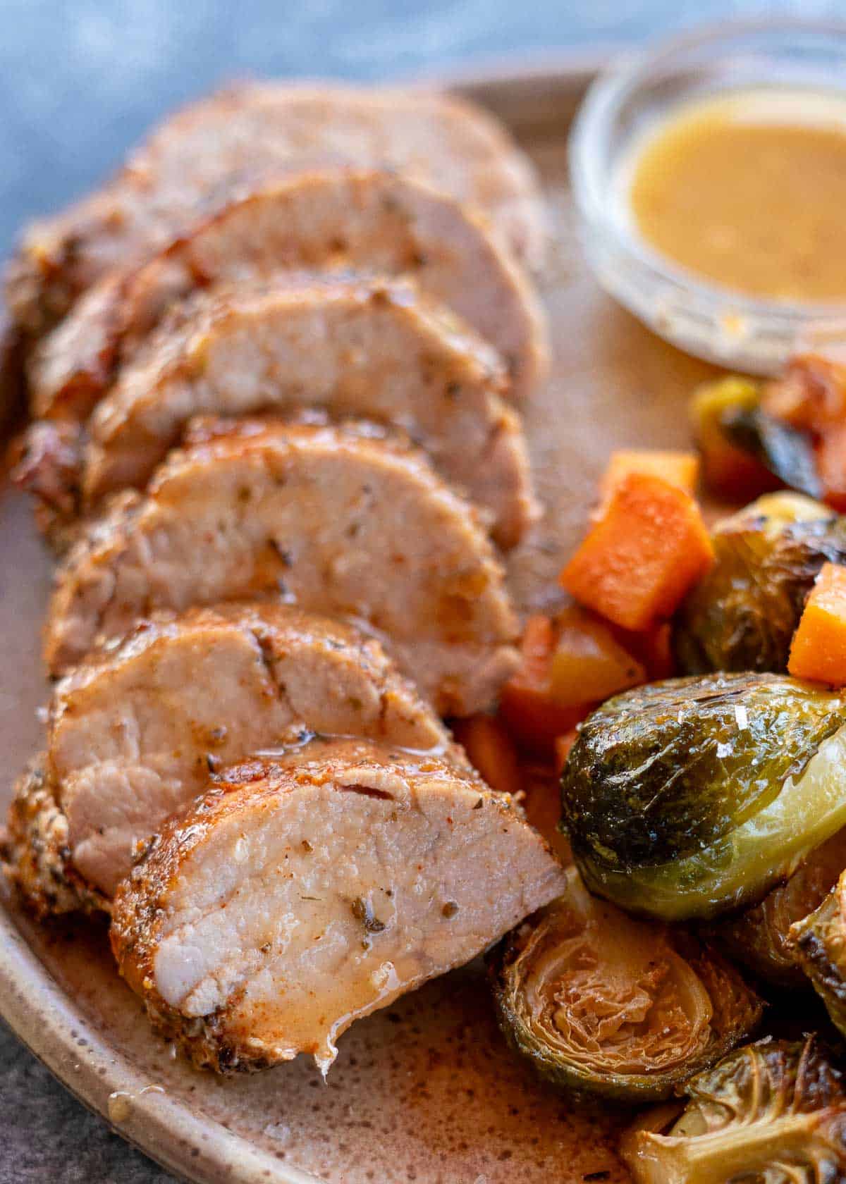 a closeup shot of a roasted pork tenderloin with juice on the plate and vegetables on the side