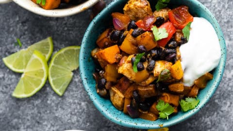 overhead shot of blue and white bowls filled with chili lime sweet potato and chicken skillet with fresh lime wedges, tortilla chips and cilantro