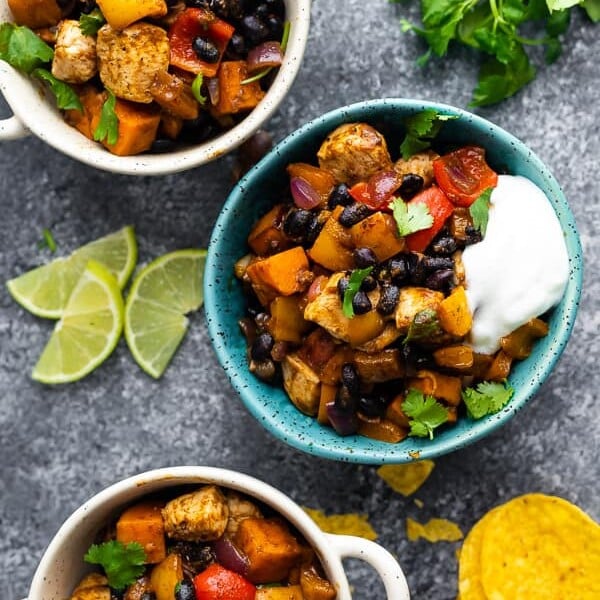 overhead shot of blue and white bowls filled with chili lime sweet potato and chicken skillet with fresh lime wedges, tortilla chips and cilantro