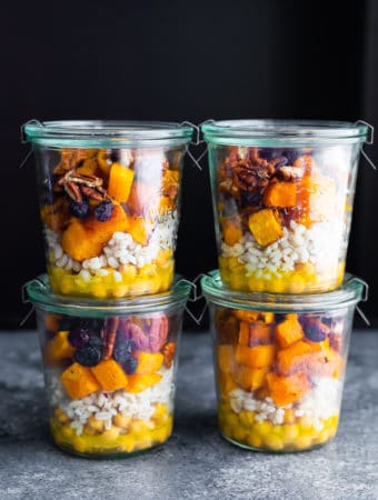 Stack of four glass jars filled with chickpea barley and butternut squash salad