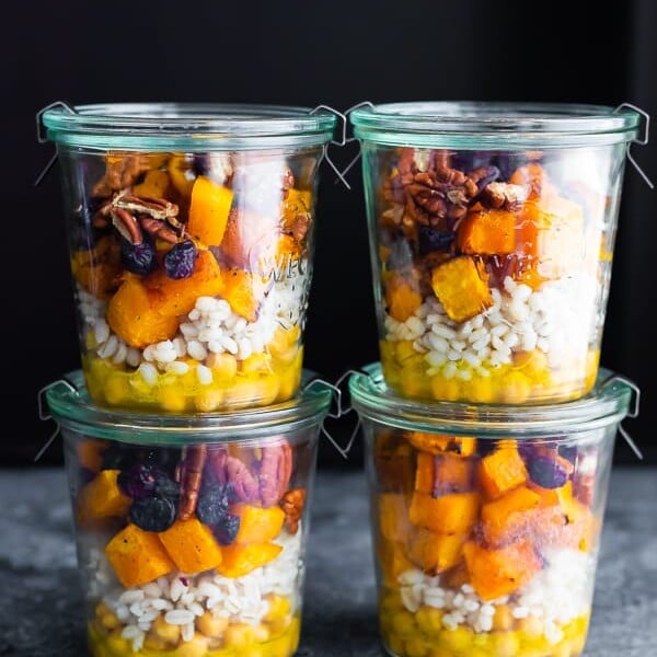 Stack of four glass jars filled with chickpea barley and butternut squash salad