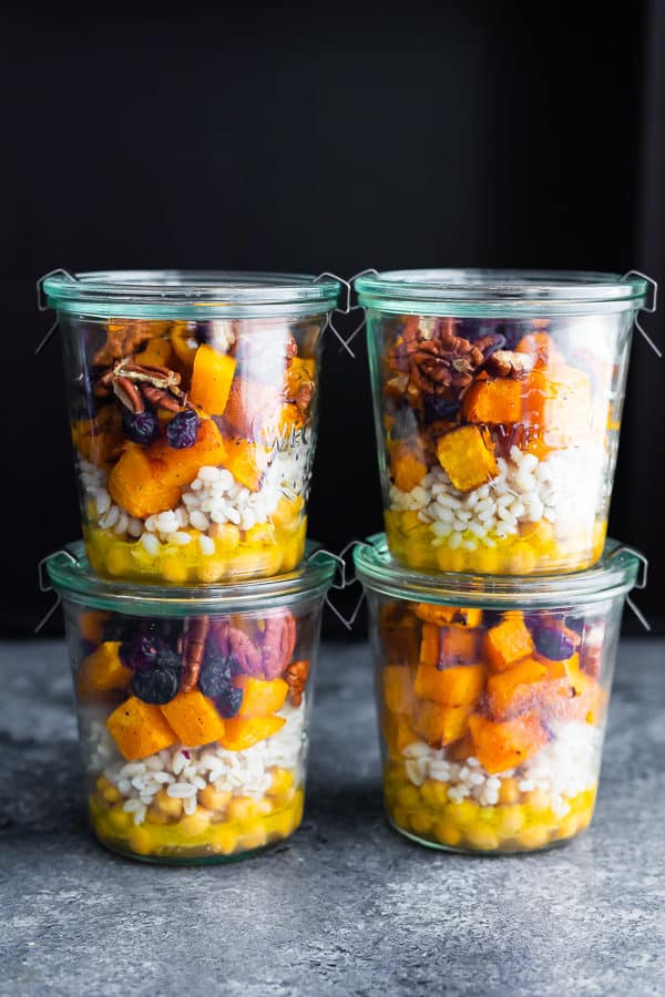 Stack of four glass jars filled with chickpea barley and butternut squash salad