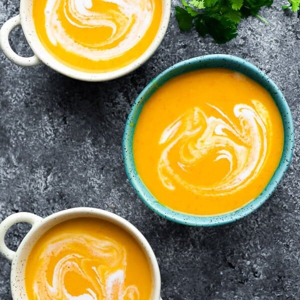 overhead shot of three blue and white bowls filled with thai butternut squash soup on gray background