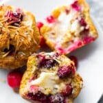 Coconut cranberry muffins cut in half on a white plate with butter on it