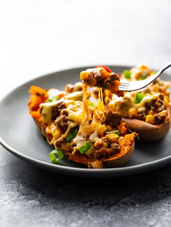 Two taco stuffed sweet potatoes on a gray plate with fork taking a bite