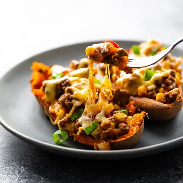 Two taco stuffed sweet potatoes on a gray plate with fork taking a bite