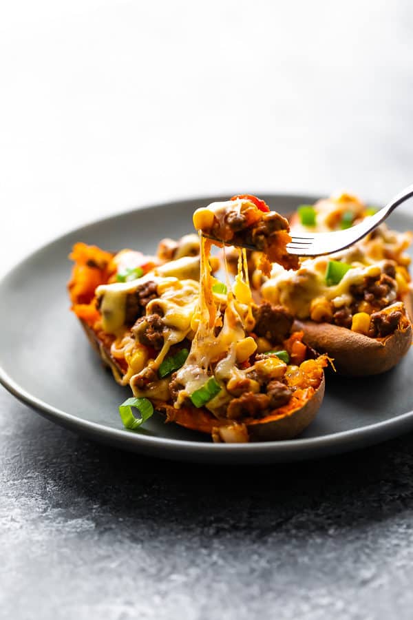 Two taco stuffed sweet potatoes on a gray plate with fork taking a bite