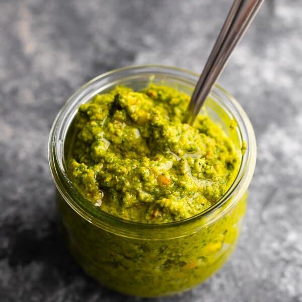 A mason jar filled with pistachio mint pesto with a spoon in it