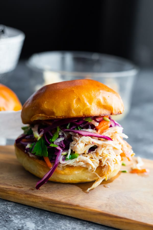 shredded chicken sandwiches sitting on cutting board with juices running down