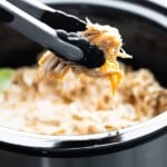 Honey lime chicken in the slow cooker with pair of tongs pulling some out