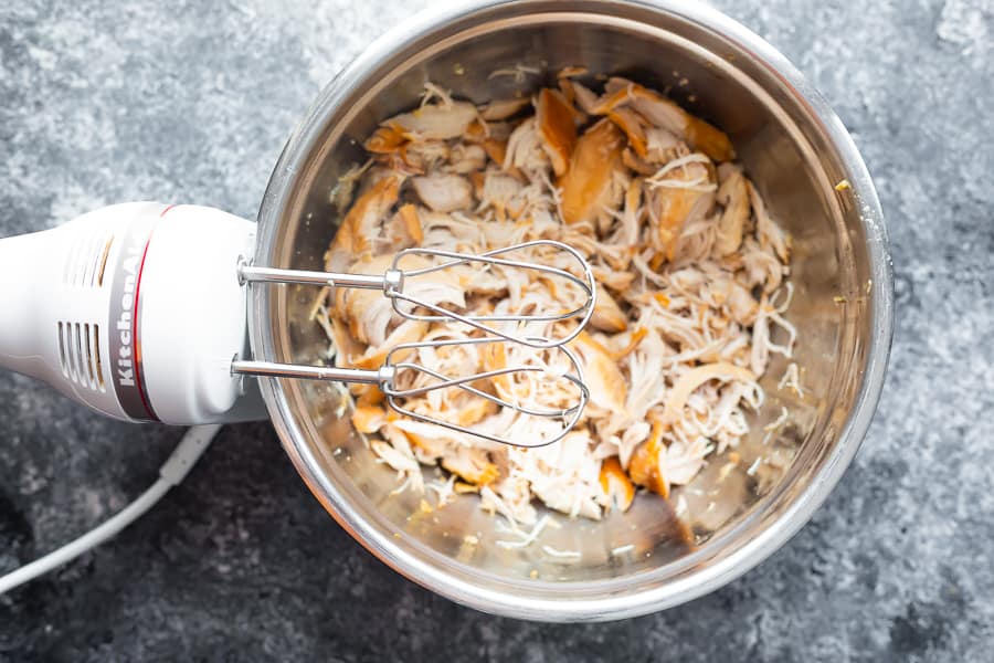 electric hand mixer over a bowl of shredded chicken