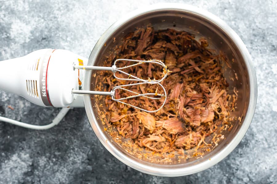hand mixer standing over bowl of shredded beef