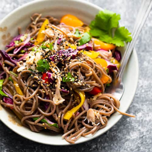 overhead shot of asian chicken soba noodle salad in white bowl with a fork