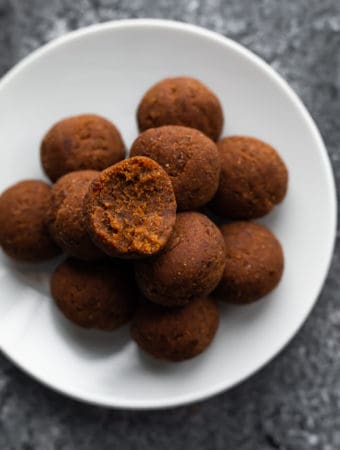 A pile of coconut date balls on a white plate with a bite taken out of one