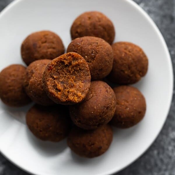 A pile of coconut date balls on a white plate with a bite taken out of one