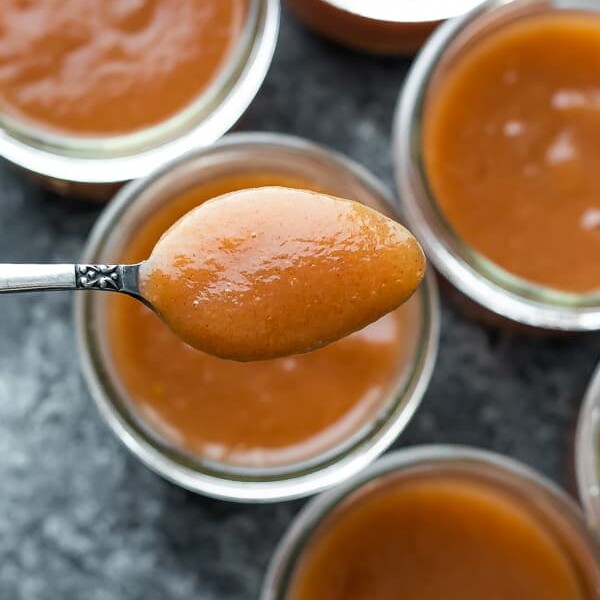 overhead shot of multiple glass jars filled with instant pot applesauce and a spoon holding a bite of it