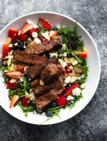overhead shot of strawberry steak salad in a large white bowl on gray background