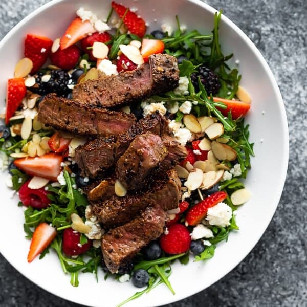 overhead shot of strawberry steak salad in a large white bowl on gray background