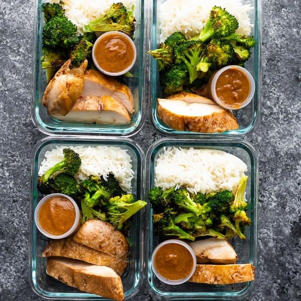 overhead shot of four glass meal prep containers filled with thai chicken lunch bowls