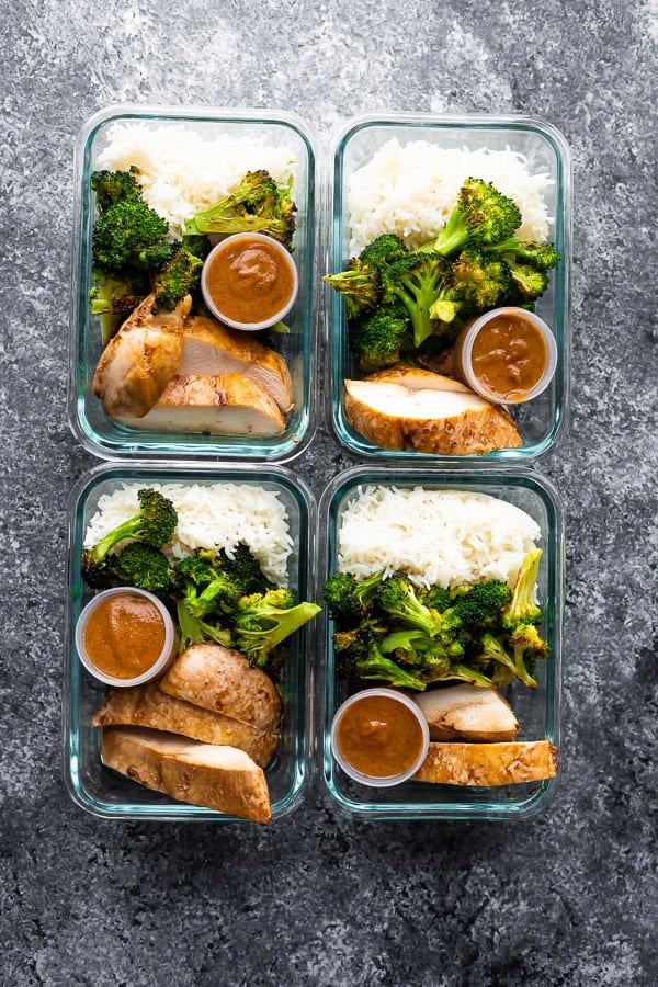 overhead shot of four glass meal prep containers filled with thai chicken lunch bowls