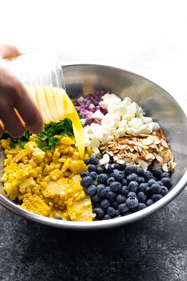 pouring vinaigrette onto the corn barley salad