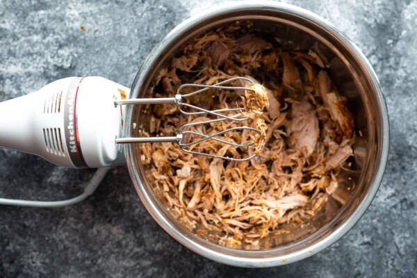 shredded pork in bowl with electric hand mixer sitting beside it