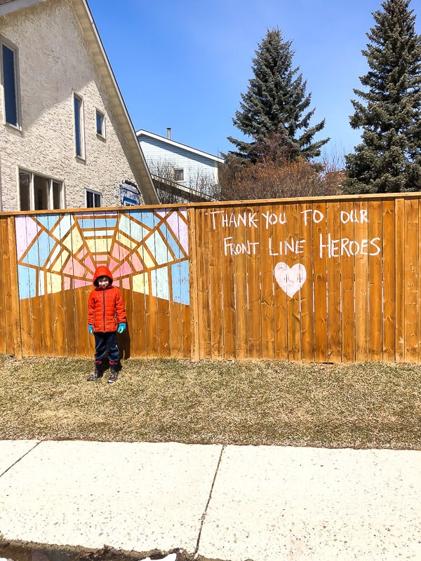kid standing in front of fence that says 'thank you to our front line heroes'