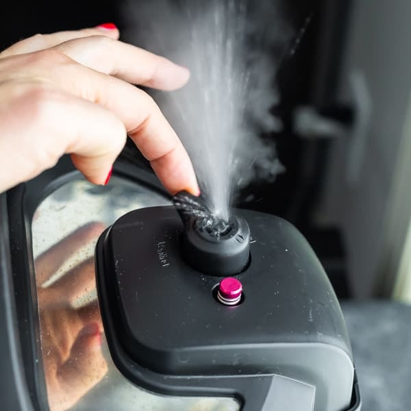 hand turning the steam release handle on an instant pot with steam coming out the valve