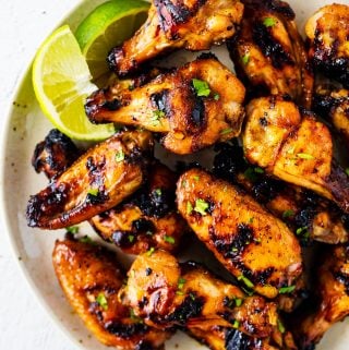 overhead view of thai grilled chicken wings on plate with lime wedges