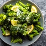 Overhead shot of a pile of broccoli with fresh lemon wedges and parmesan on a gray plate