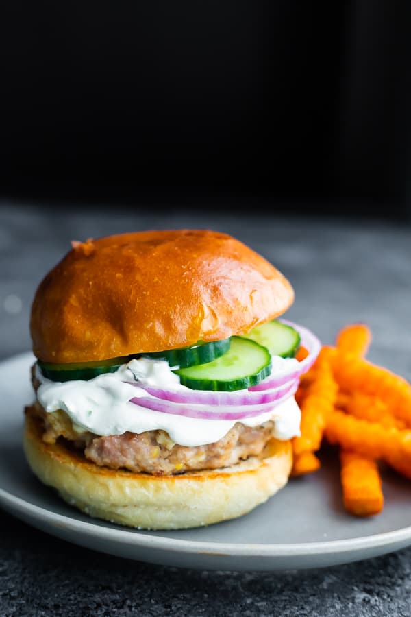 side angle view of a Greek turkey burger on a plate with sweet potato fries