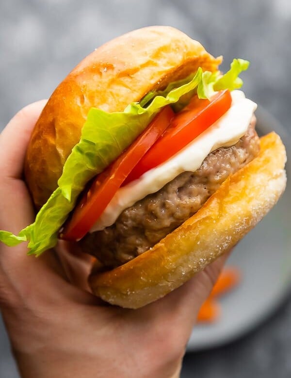 hand holding up a perfect juicy turkey burger with lettuce and tomato slices