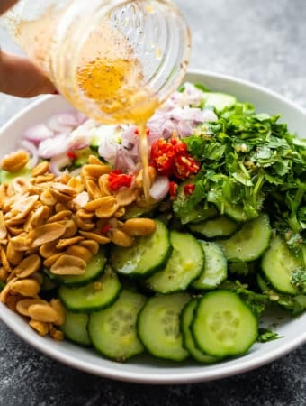 Crunch Asian cucumber salad in a white bowl with dressing in a mason jar being drizzled on top