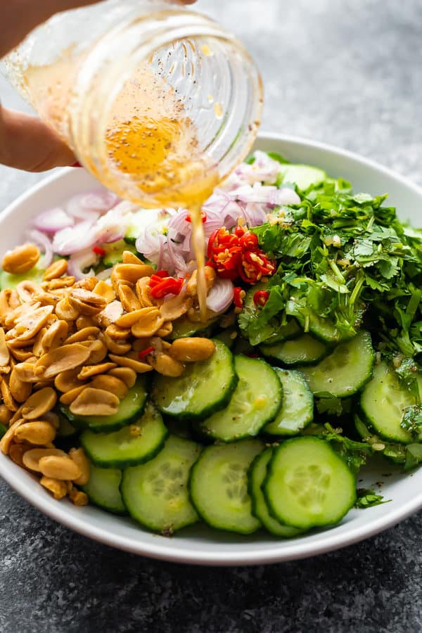 Crunch Asian cucumber salad in a white bowl with dressing in a mason jar being drizzled on top