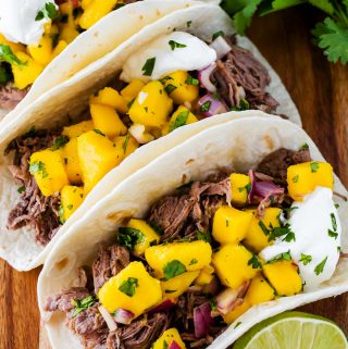 three jerk beef tacos with mango salsa on a cutting board