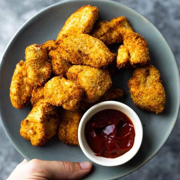 hand holding a plate of air fryer chicken nuggets