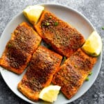 overhead view of plate with four air fryer salmon portions and lemon wedges