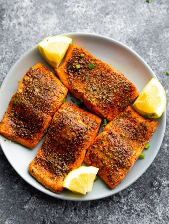 overhead view of plate with four air fryer salmon portions and lemon wedges