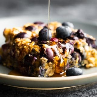 close up shot of a slice of blueberry baked oatmeal with syrup drizzled on top